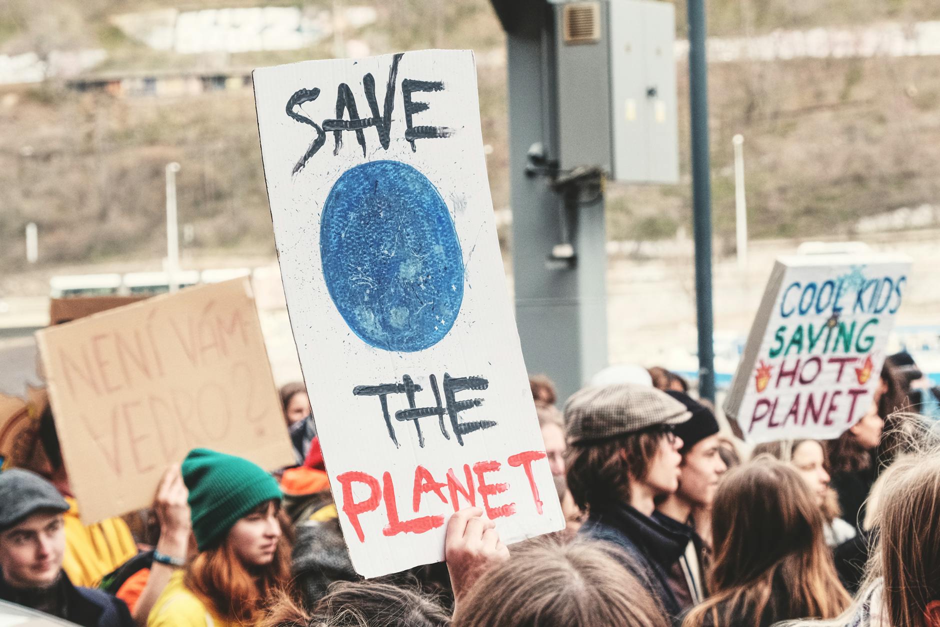 A climate change protest in Prague, with people holding environmental signs like 'Save the Planet'.