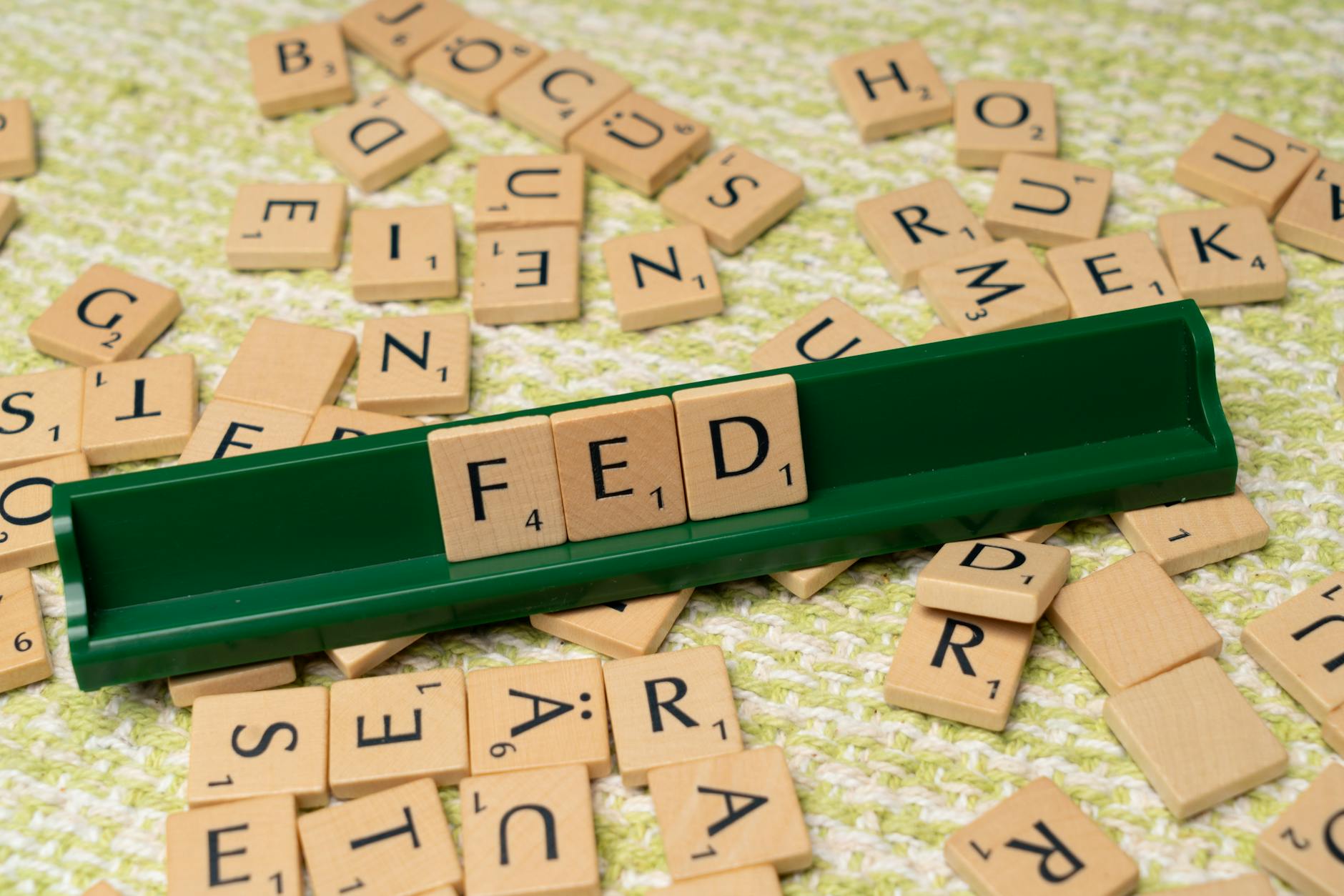 Scrabble tiles spelling 'FED' on a green rack surrounded by scattered tiles on a textured surface.