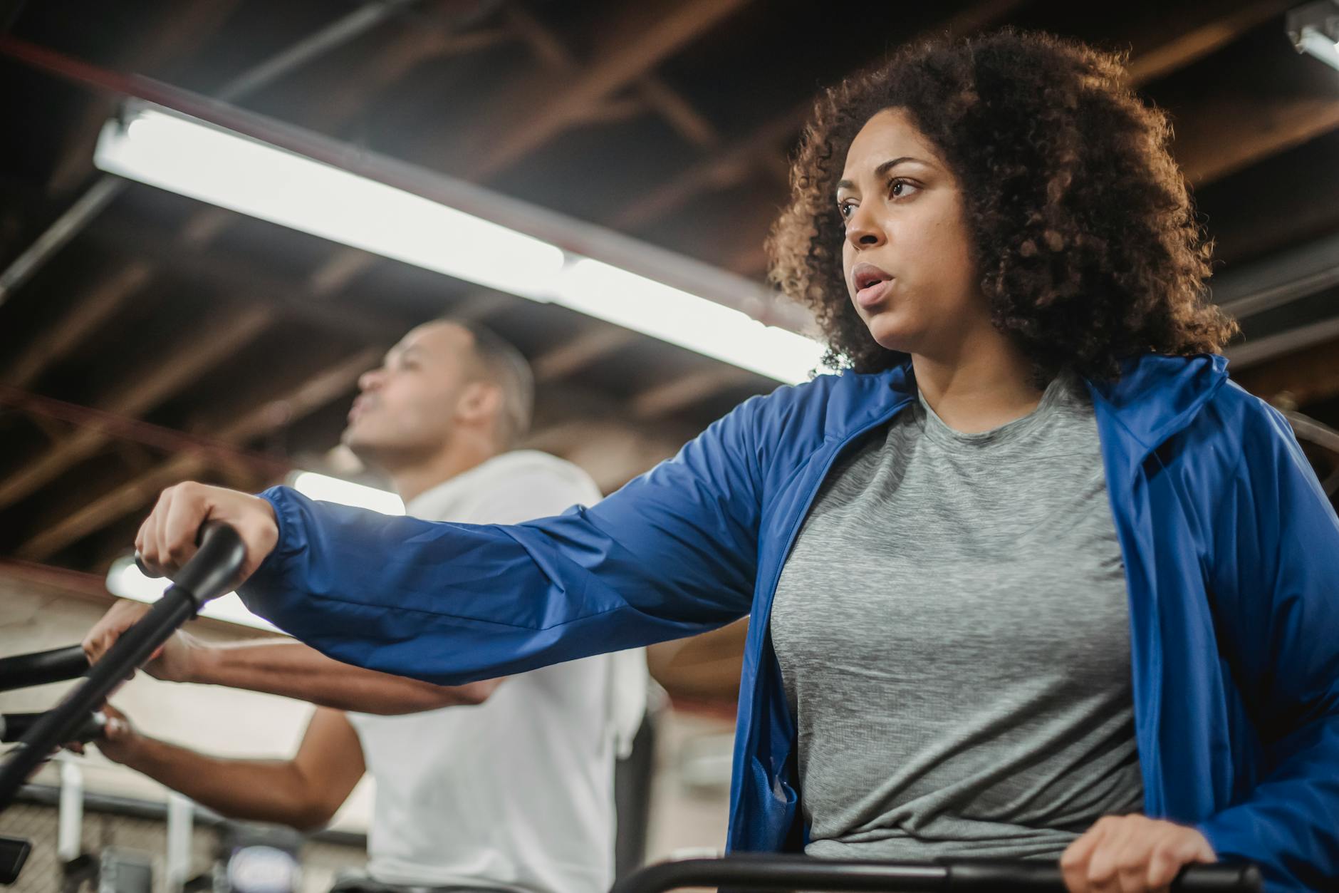 A woman and man intensely working out on stationary bikes indoors at a gym, demonstrating focus and determination.