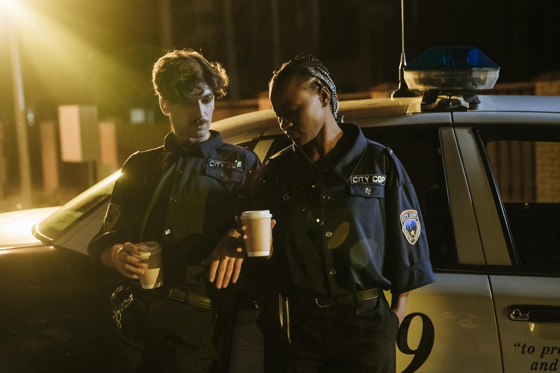 Two police officers enjoying a coffee break beside their patrol car during a night shift.